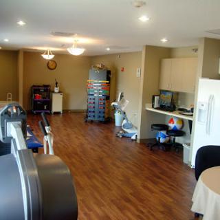 A spacious and well-lit room featuring exercise equipment and a kitchenette area.