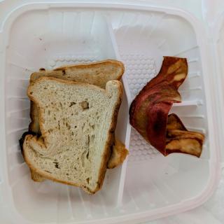 A simple meal with a sandwich and bacon in a plastic container.