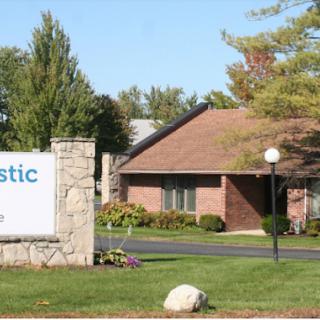 A welcoming entrance to a facility, featuring well-maintained landscaping and a clear sign.