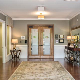 A beautifully decorated entrance foyer with wooden doors, a decorative rug, and elegant lamps.