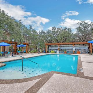 A serene outdoor swimming pool surrounded by trees with lounge chairs and sun umbrellas.
