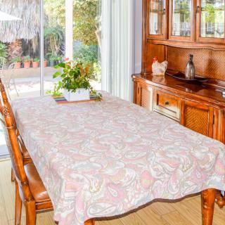 A cozy dining room with a table covered by a patterned tablecloth, surrounded by wooden chairs, and a cabinet in the background.