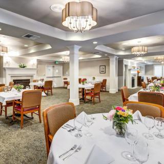 An elegant dining area with neatly arranged tables and chairs, featuring chandeliers and tasteful decor.