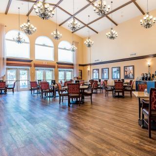 A spacious dining area with chandeliers, wooden flooring, and natural light from large windows.