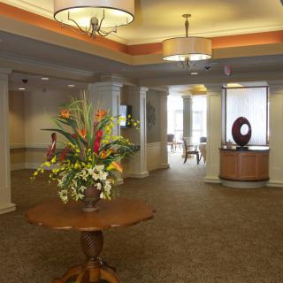 A well-decorated lobby featuring a central table with a floral arrangement, elegant lighting fixtures, and inviting interior decor.