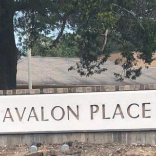 A sign for Avalon Place located outdoors near trees and a building.
