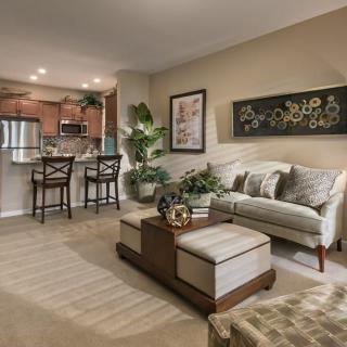 A cozy open-concept living room with a kitchen area, featuring a sofa and bar stools.