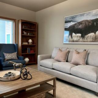 A cozy living room featuring a comfortable sofa, an armchair, and a stylish coffee table with decorative items. A large artwork hangs on the wall above the couch.