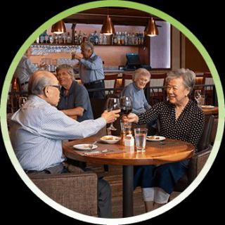 A group of elderly people enjoying a meal and toasting with wine glasses in a restaurant setting.