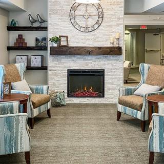 A cozy living room with armchairs and a modern fireplace set against a stone wall.