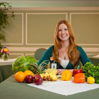 A woman sits at a table surrounded by various fruits and vegetables, promoting healthy eating.