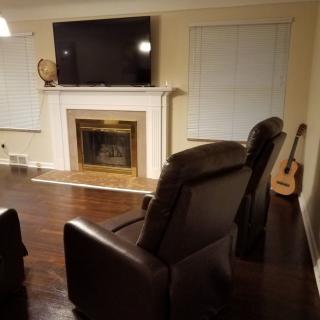 A cozy living room with a fireplace, TV, armchairs, and a guitar against a wooden floor.