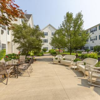 A cozy outdoor patio area with chairs and tables surrounded by trees and apartment buildings.