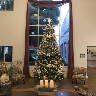 A beautifully decorated Christmas tree stands in a spacious room, adorned with lights and ornaments, accompanied by glowing candles.