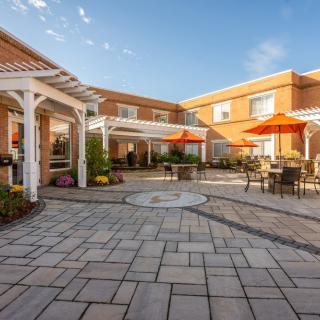 A sunny courtyard with outdoor seating and umbrellas, surrounded by a brick building.