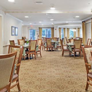 A spacious dining room with multiple tables and chairs, featuring a carpeted floor and large windows.