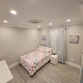 A modern and minimalist bedroom featuring a single bed with floral bedding, light wooden floors, and simple decor.