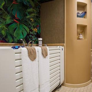 A stylish bathroom featuring a tropical-themed wall, white radiators with towels, and decorative niches.