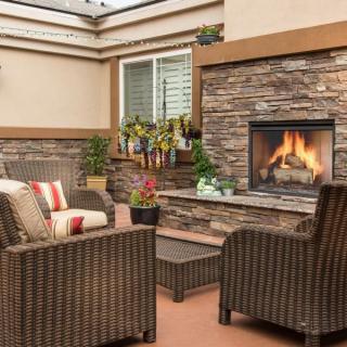 A cozy outdoor patio with wicker furniture and a stone fireplace.