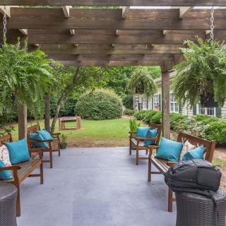 A cozy outdoor patio with a pergola and hanging plants, featuring comfortable seating and garden views.