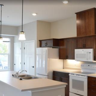 A modern kitchen featuring a central island counter and wooden cabinetry, equipped with white appliances and pendant lighting.