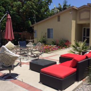 A sunny backyard patio with red cushioned furniture and an umbrella.