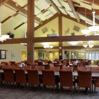 A spacious dining area with long tables and cushioned chairs, featuring high ceilings and elegant chandeliers.