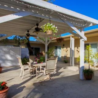 A sunny backyard patio with a pergola, outdoor furniture, and hanging plants.