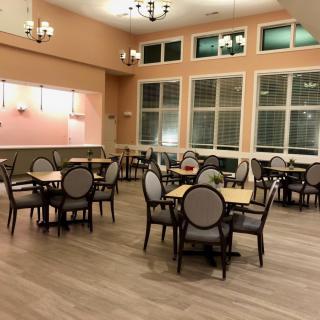 An elegant dining room with multiple tables and chairs, warmly lit by chandeliers.