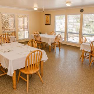 A cozy dining room with wooden tables and chairs, set with white tablecloths.