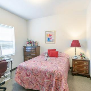 Cozy bedroom with a pink bedspread, dresser, and table lamp.