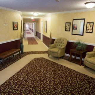 A hotel hallway with a seating area, featuring two armchairs, a side table, and decorative wall art.