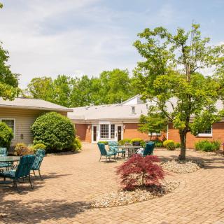 A peaceful outdoor patio area with tables and chairs surrounded by trees and a brick building.
