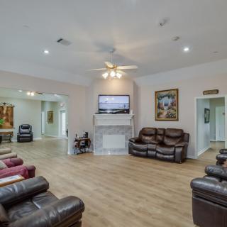 A cozy living room with leather sofas, a central fireplace and television, surrounded by artwork and illuminated by a ceiling fan.