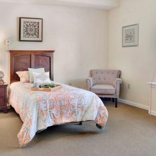 A cozy bedroom featuring a single bed with decorative bedding, a comfortable chair, and stylish artwork.