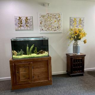 A cozy living room corner featuring a fish tank, vibrant artwork, and a vase of yellow flowers.