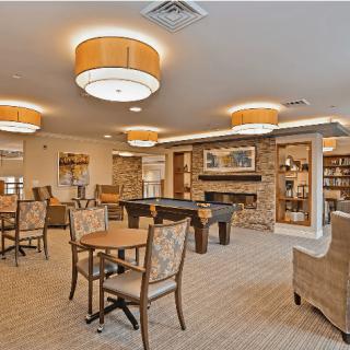 A cozy lounge area with tables, chairs, and bookshelves under warm lighting.