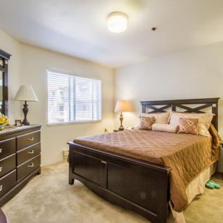 A cozy bedroom featuring a large bed, dresser, and lamps, with natural light from the window.