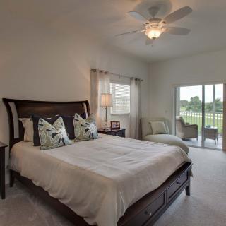 A cozy bedroom featuring a wooden bed with decorative pillows, a ceiling fan, and a view of the outdoors through sliding doors.