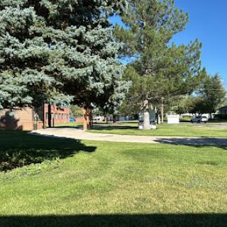 A serene view of a residential area featuring lush green grass and trees under a clear blue sky.