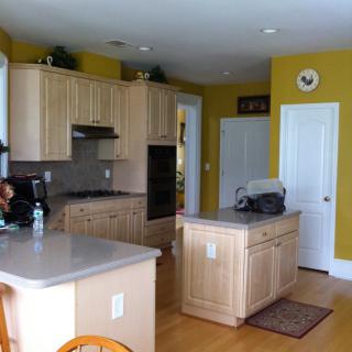 A kitchen with wooden cabinets and yellow walls, featuring a central island and modern appliances.