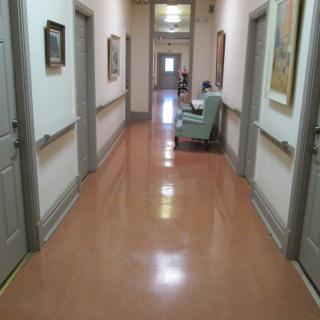 A well-lit hospital hallway with doors on either side and a chair at the end.
