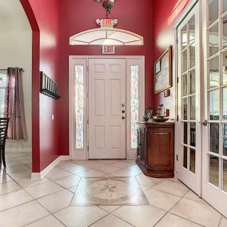 A bright entryway with red walls and a white door, featuring tiled flooring and a chandelier.