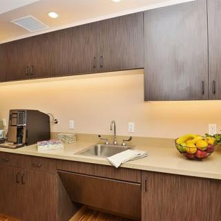 A modern kitchen with wooden cabinets, a coffee maker, a fruit bowl on the counter, and under-cabinet lighting.