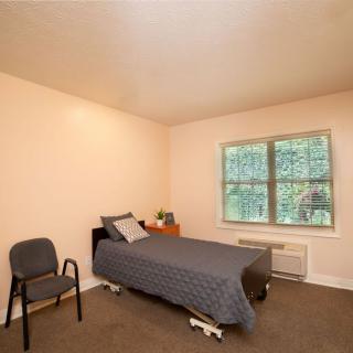 A minimalist bedroom with a single bed, chair, and window overlooking greenery.