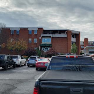 A view of a parking lot filled with various cars, next to a brick building under a cloudy sky.