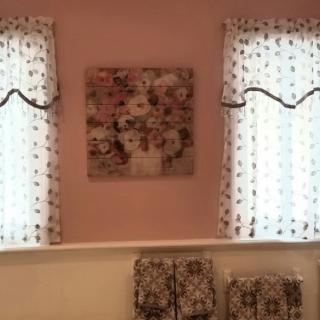 A cozy room featuring two windows with floral curtains and a central floral wall art piece.
