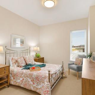 A cozy bedroom with a decorative bedspread, wooden furniture, and a window allowing natural light.