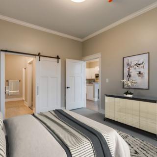 A modern bedroom with neutral tones, featuring a bed, dresser, and sliding barn door leading to an adjacent room.