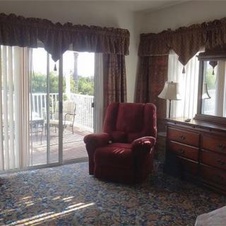 A cozy living room with a red armchair, dresser, and access to a balcony through sliding glass doors.